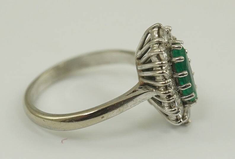 A modern 18ct white gold and single stone marquise cut emerald set ring, bordered with round brilliant cut diamonds